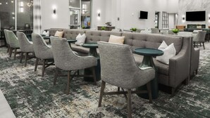 A modern lounge area with a sofa, chairs, and tables, featuring a marble wall and a flat-screen TV.