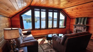 A cozy cabin interior with a large window, a fireplace, and leather furniture. - Lakeview Suites (Bolton Landing)