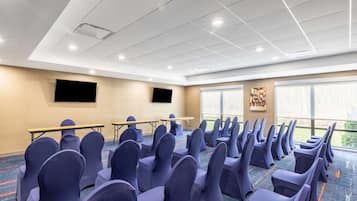 A conference room with rows of chairs, a projector screen, tables, and large windows.