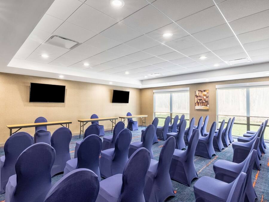 A conference room with rows of chairs, a projector screen, tables, and large windows.