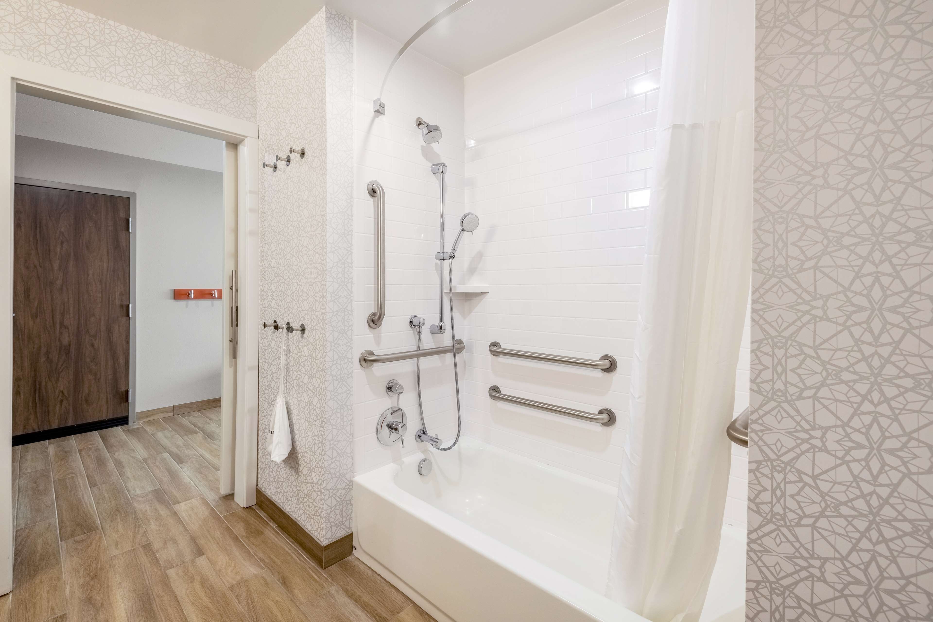 Un bagno moderno con doccia a ingresso senza barriere, maniglie di sostegno e vasca da bagno bianca.