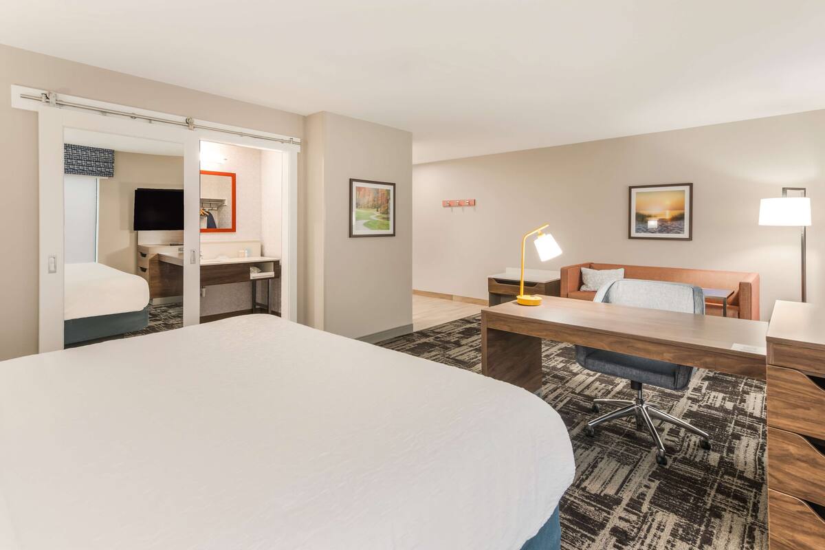 A hotel room with a large bed, a desk with a chair, a sofa, and a TV.