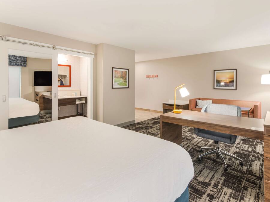 A hotel room with a large bed, a desk with a chair, a sofa, and a TV.