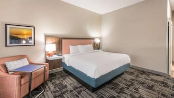 A hotel room with a bed, a desk, a chair, a nightstand, a lamp, and a framed picture on the wall.