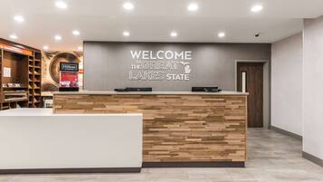 A reception desk with a wooden panel design, a sign reading "WELCOME TO THE GREAT LAKES STATE," and a view of the lobby area with a door and a security camera on the ceiling.