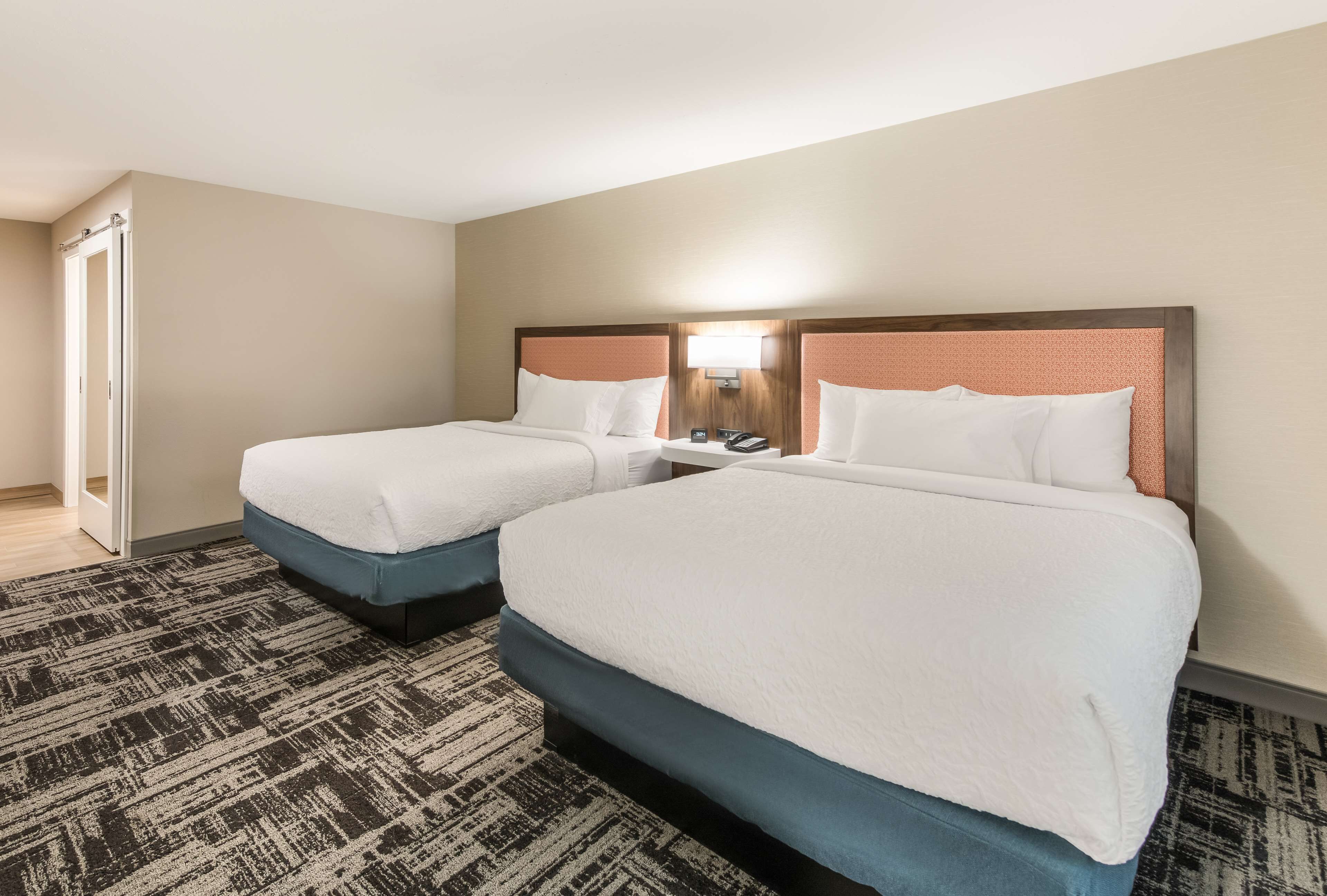 A hotel room with two beds, a carpeted floor, and a door to a bathroom.