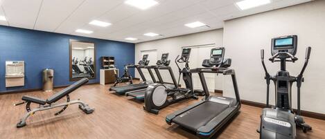 Une salle de sport équipée de plusieurs tapis de course, de plusieurs appareils elliptiques et d’un banc de musculation.