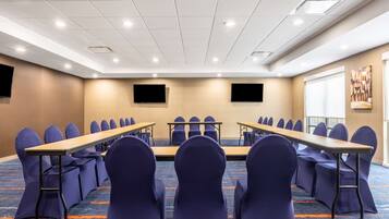 A conference room with long tables and chairs, a carpeted floor, and a white ceiling with recessed lighting.