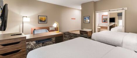 A hotel room with two beds, a desk with a lamp, a chair, a TV, and a mirror.