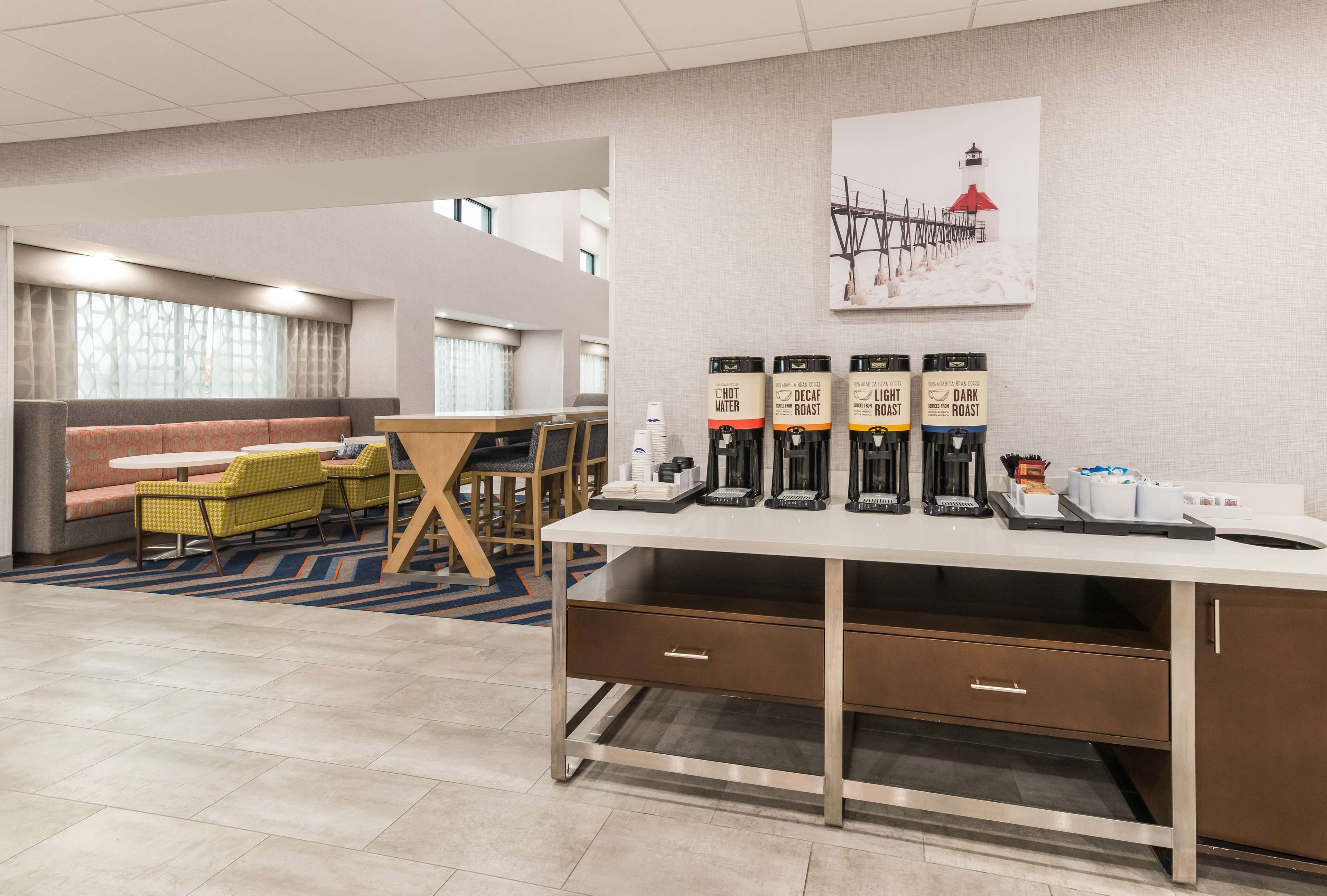 A hotel lobby with a seating area, a coffee station, and a painting on the wall.