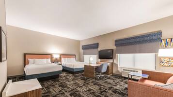 A hotel room with two beds, a desk, a chair, a TV, and a window with blinds.