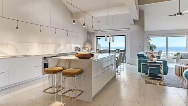 Une cuisine moderne dotée d’un îlot central, de tabourets de bar, de luminaires suspendus et offrant une vue sur l’océan.