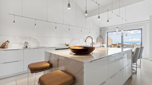 Une cuisine moderne dotée d’un grand îlot central, de meubles blancs et d’un éclairage suspendu.