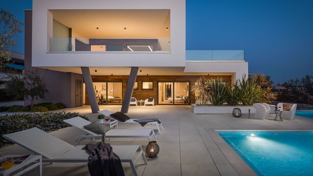 Una casa moderna de dos pisos con piscina, mobiliario exterior y un interior bien iluminado.