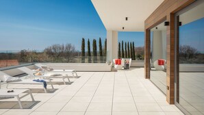 Amplia terraza en la azotea con sillones de sol, una mesa con bebidas y vistas del paisaje.