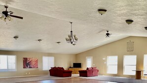 Um quarto amplo com teto alto, várias ventoinhas no teto, um candelabro e uma janela grande.