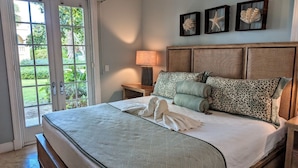 Una camera da letto con un letto grande, un comodino con una lampada e vista su un giardino attraverso una porta vetrata.
