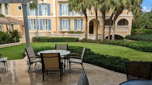 Un patio con un tavolo e sedie rotonde, vista su un edificio con persiane blu e un prato curato.