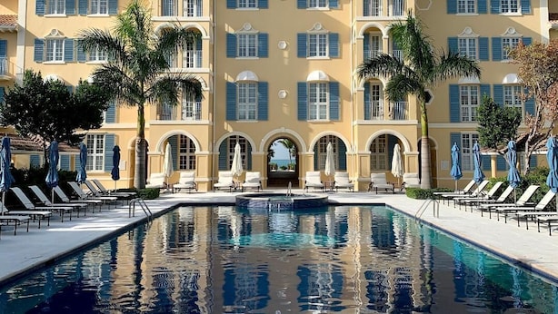 Un grande hotel con piscina, numerosi balconi e palme.