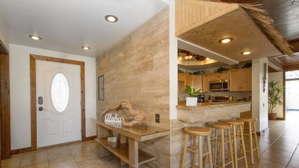 A modern kitchen with a central island, bar stools, and a wooden bench. - Royal Waikiki Penthouses (Honolulu)