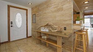 A modern interior with a wooden bench, a glass table with 'Aloha' signage, and a door with a decorative glass panel. - Royal Waikiki Penthouses (Honolulu)