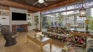 A spacious living room with a wooden ceiling, a large TV, a fireplace, and a tropical-themed sofa. - Royal Waikiki Penthouses (Honolulu)