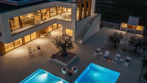 Una moderna casa a più piani con piscina, area salotto esterna e patio ben illuminato.