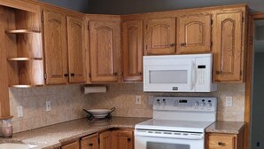 Une cuisine avec des meubles de rangement en bois, un four à micro-ondes, une cuisinière et un sol carrelé.