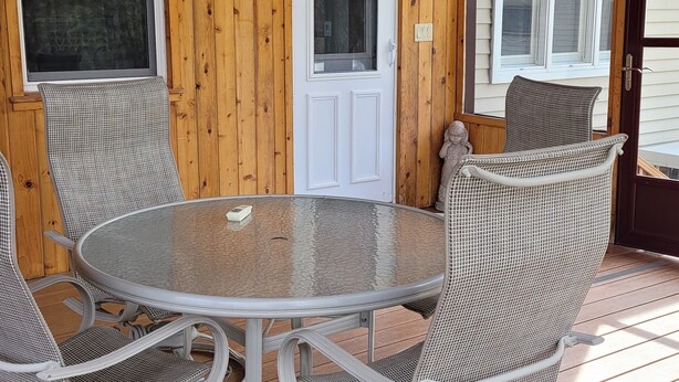 Une terrasse en bois avec une table ronde en verre et des chaises en osier.