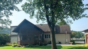 Une maison dotée d’un grand porche grillagé, d’un arbre dans le jardin et d’une pelouse bien entretenue.