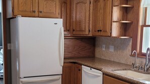 Une cuisine avec des meubles en bois, un réfrigérateur blanc, un lave-vaisselle et un plan de travail en granit.
