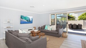 A modern living room with grey sofas, a wooden coffee table, and a TV displaying a wave.