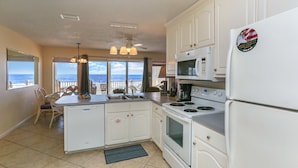 A kitchen with white cabinets, a stove, microwave, and refrigerator. There is a view of the ocean through large windows. - Beach front, updated townhome in Indian Pass~ Pelican Landing 2 (Indian Pass)