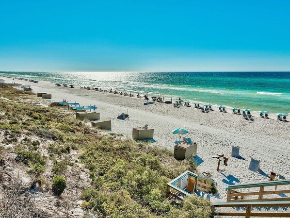 A beach with sun loungers, umbrellas, and a clear view of the ocean.