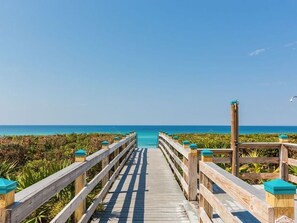 A wooden boardwalk leading to a beach with clear blue water and a clear sky.