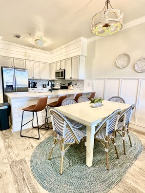 A modern kitchen with white cabinetry, a central island, and a dining area with a table and chairs. - Sleeps 8, Steps to Rosemary, heated pool, deeded beach access, shopping, dining! (Seacrest)