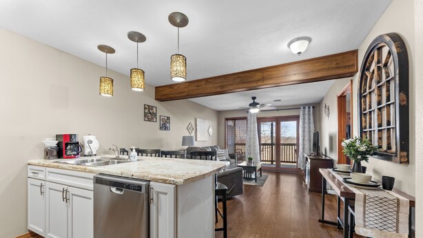 Une cuisine dotée d’un îlot central, de meubles blancs, d’appareils électroménagers en acier inoxydable, de luminaires suspendus et d’une poutre en bois au plafond.