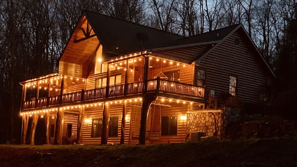 Une cabane en rondins dotée d’un balcon et illuminée de guirlandes lumineuses.