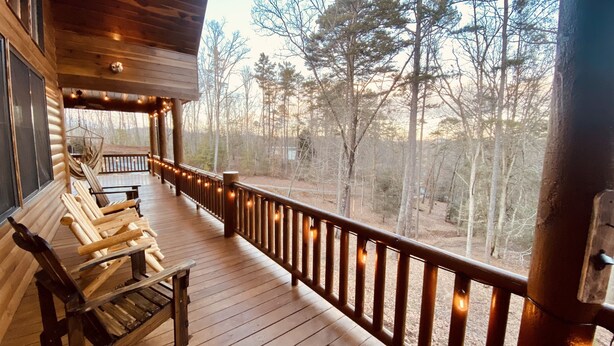 Une terrasse en bois, dotée d’une rambarde et illuminée de guirlandes lumineuses, qui offre une vue sur une forêt.