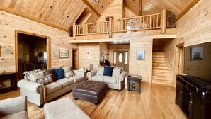 L’intérieur de cette vaste cabane en rondins comprend une chambre à coucher située en mezzanine, un salon avec deux canapés et une table basse, ainsi qu’un coin cuisine.