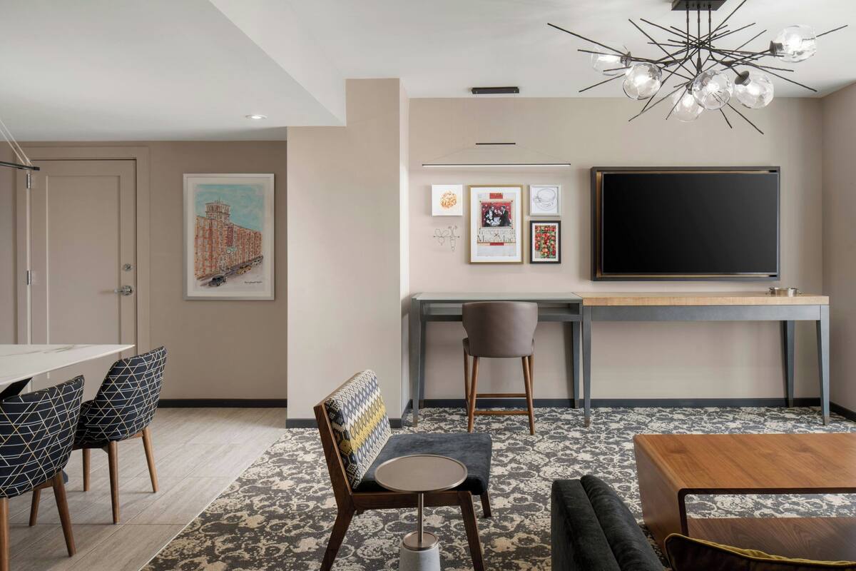 A modern room with a dining area, a sofa, a TV, and a patterned carpet.