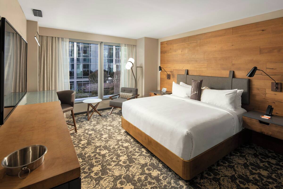 A hotel room with a large bed, a desk, a chair, a small table, and a window with curtains.