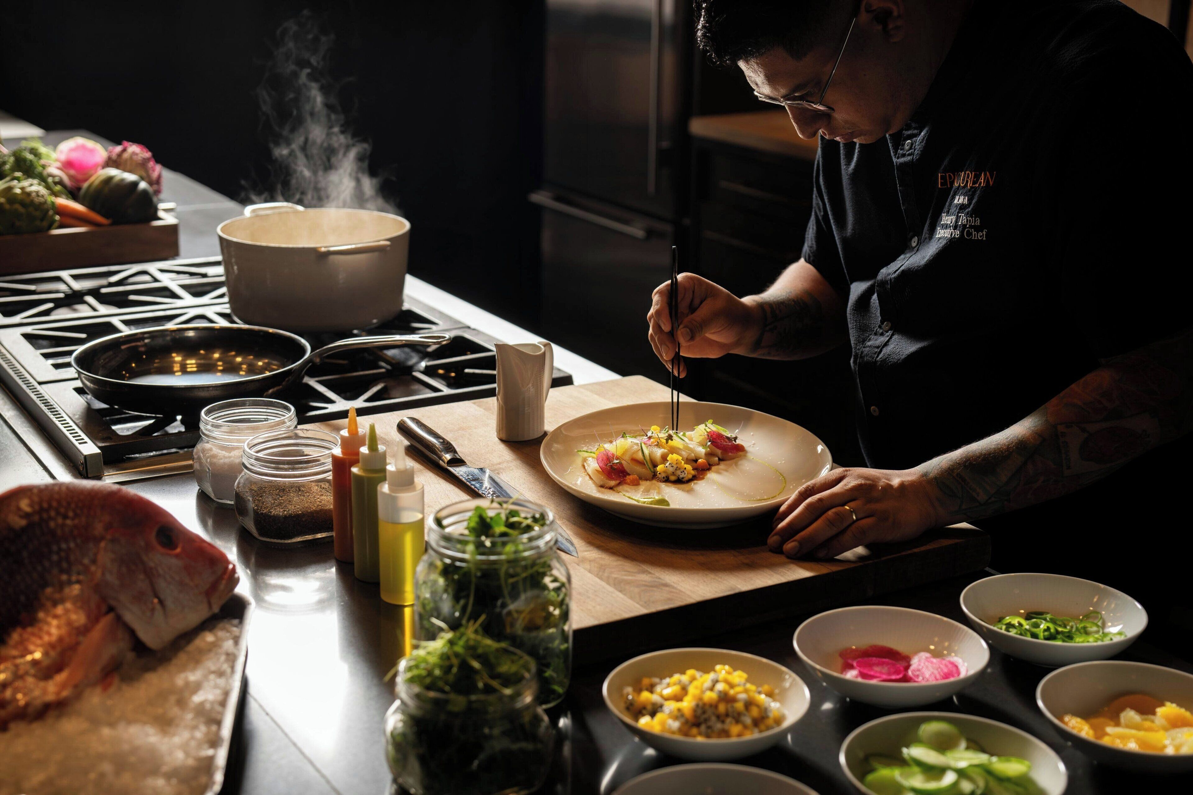 A chef preparing food in a kitchen with various ingredients and cooking utensils visible.
