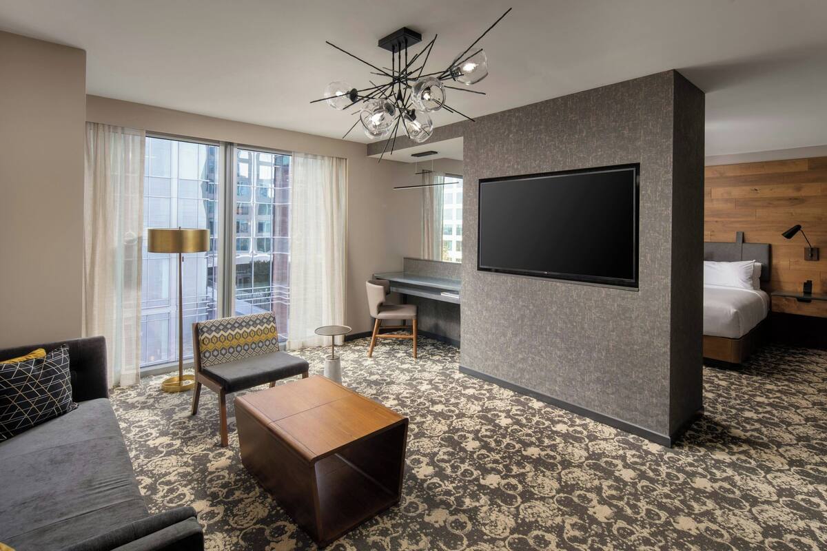 A modern hotel room with a large TV, a sofa, a desk, and a bed.