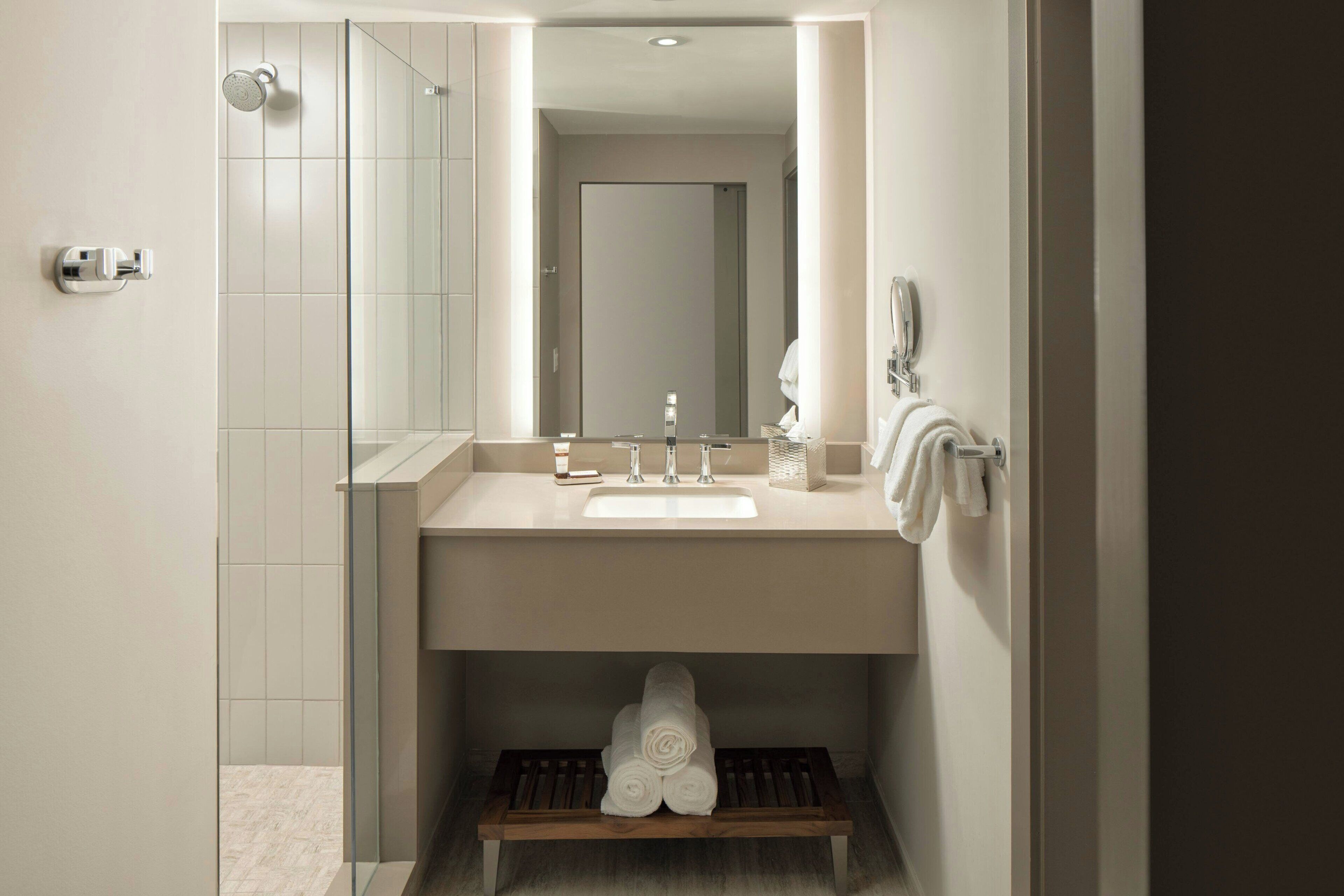 A modern bathroom with a glass shower enclosure, a sink with a mirror above it, and a towel rack with towels.