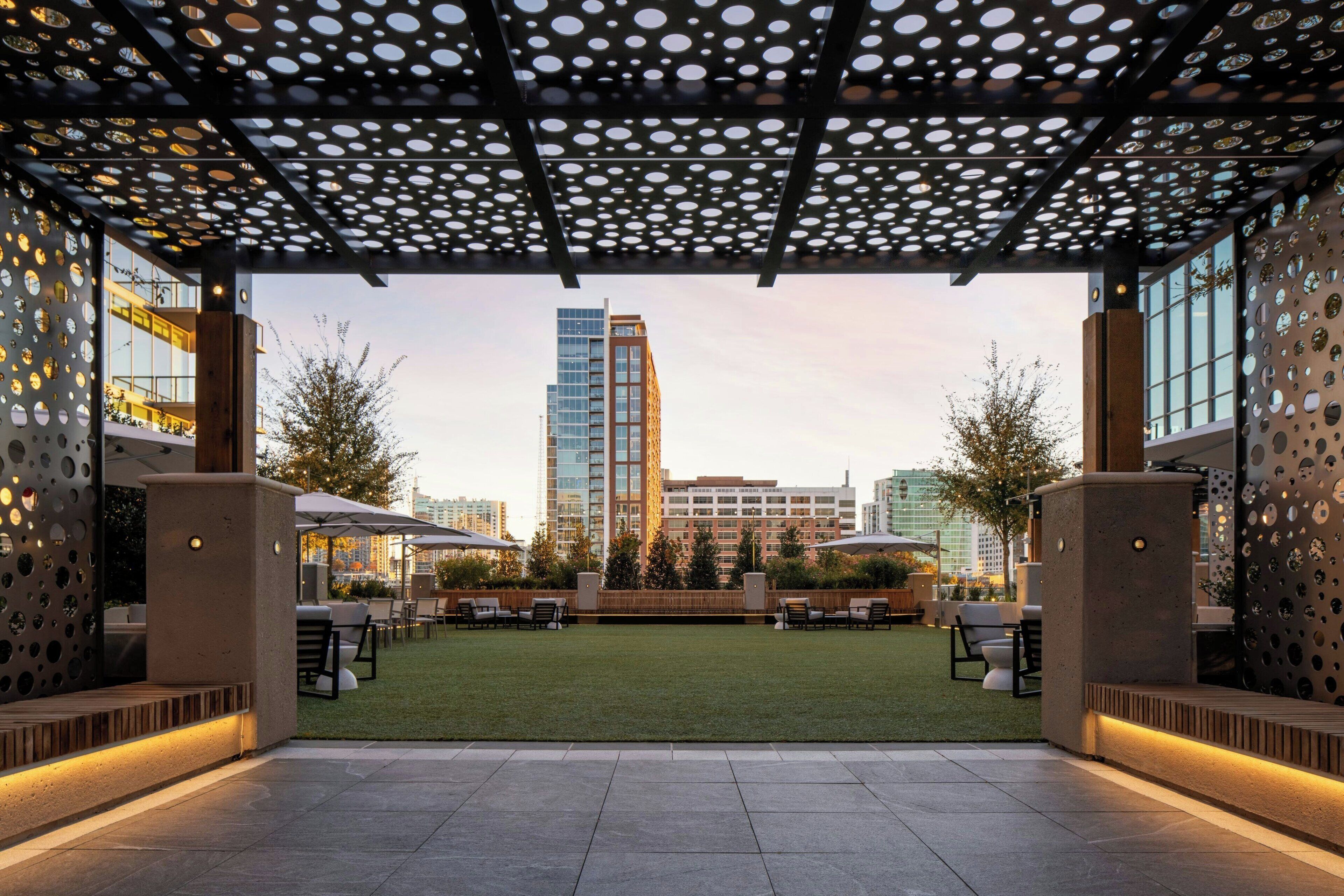 An outdoor patio area with a view of a tall building, furnished seating, and a well-maintained lawn.