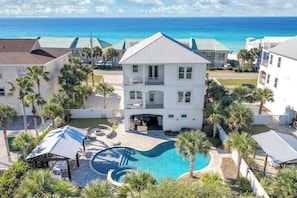 A two-story building with a swimming pool, surrounded by palm trees and a view of the ocean.