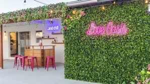 A cozy outdoor seating area with a neon sign reading "Love Oasis" and a wall covered in greenery.