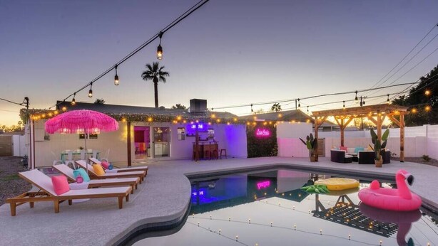 A pool area with lounge chairs, a pink flamingo float, and string lights.