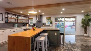 A modern kitchen with a wooden island, bar stools, and a view of an outdoor area.